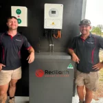 Two technicians in Bright Spark Group uniforms standing next to a RedEarth energy storage system.