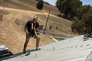 With a safety harness attached, an electrician stands on a metal roof in a rural setting and ensures a secure installation
