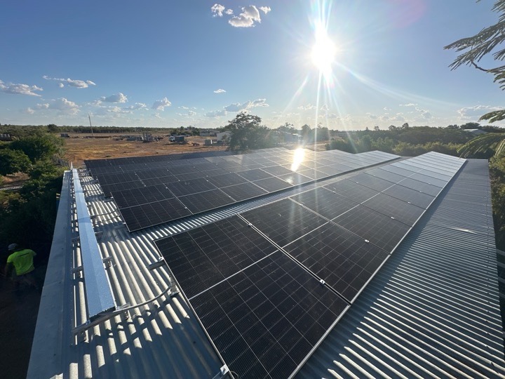 Solar panel array catching the sun on a wide roof with scenic countryside views in the background.