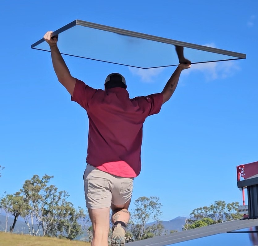 Bright Spark Group technician lifting a solar panel onto a rooftop in a rural area., Hassle free installations
