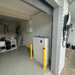 Compact solar battery unit installed inside a garage with safety bollards for protection.