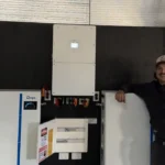 Compact multi-unit solar battery and inverter setup mounted on an internal wall, partially visible technician nearby.