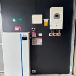 Wall-mounted solar inverter system with dual battery storage units installed indoors against a dark panel.