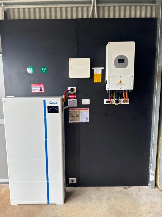 Wall-mounted solar inverter system with dual battery storage units installed indoors against a dark panel.