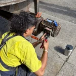 Electrician performing maintenance work on residential electrical with equipment, wearing high-visibility safety gear.