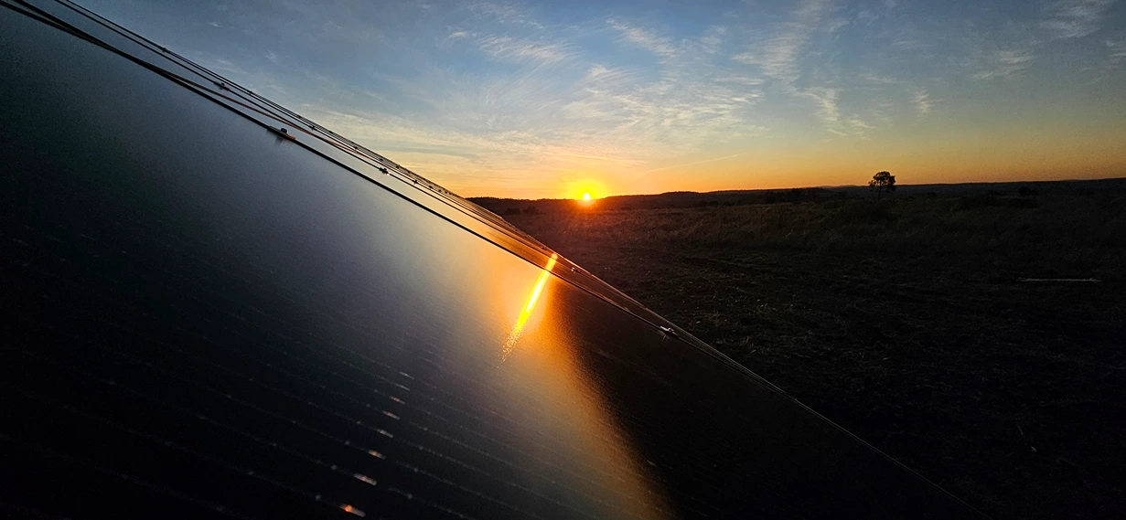Clean solar panel reflecting a vibrant sunset over a rural landscape.