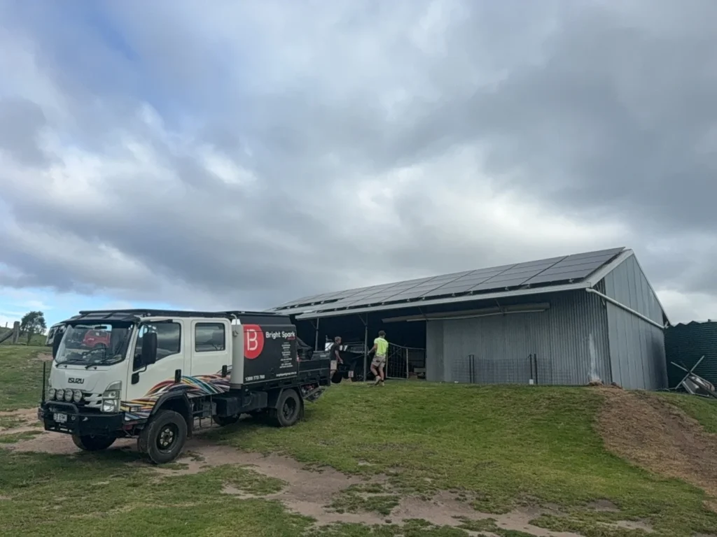 Solar panel installation on rural farm shed roof by Bright Spark Group with service vehicle onsite for renewable energy system setup.