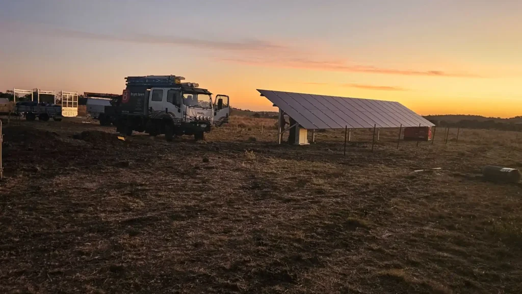 Rural ground-mounted solar panel installation with Bright Spark truck on farmland at sunset