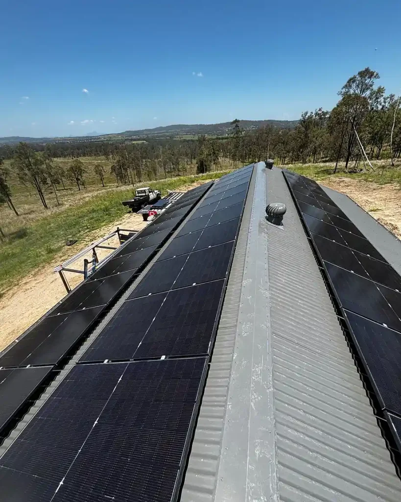 Rural rooftop solar panel installation on a metal shed roof overlooking farmland under a stormy sky
