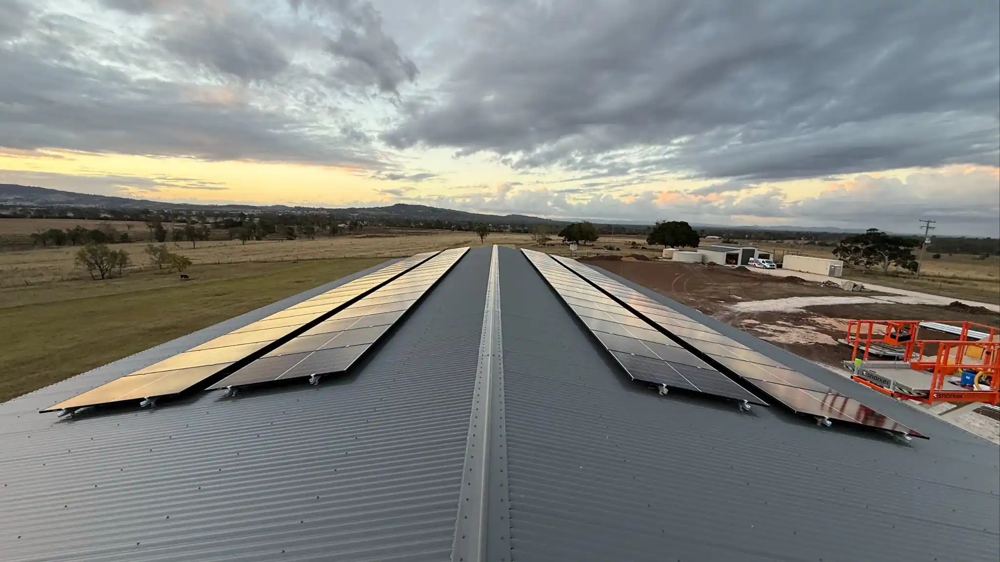 Rural rooftop solar panel installation on a metal shed roof overlooking farmland under a stormy sky
