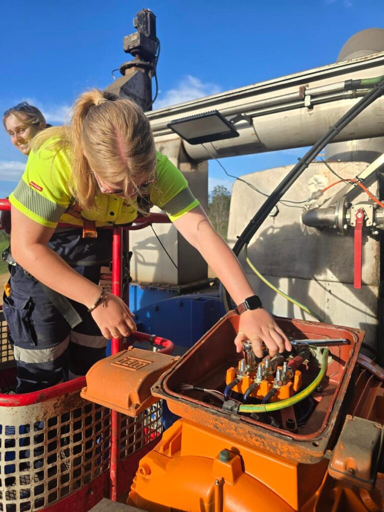 Electrician wiring a three-phase motor terminal box from an elevated work platform