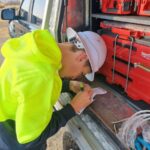 Electrician completing paperwork beside a work ute