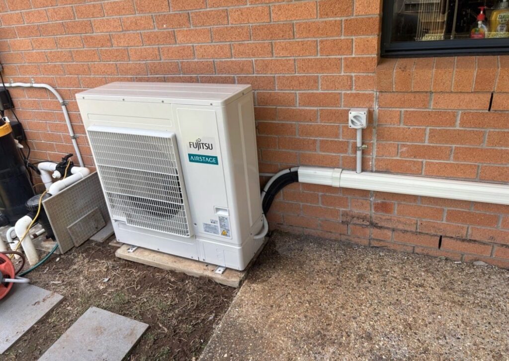 Large Fujitsu Airstage air conditioning outdoor unit installed beside a brick home