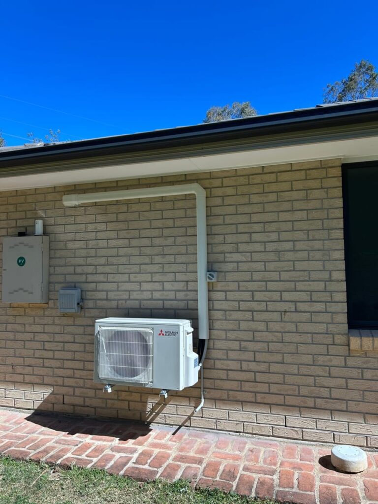 Mitsubishi Electric outdoor unit installed on a brick home beside a solar PV box