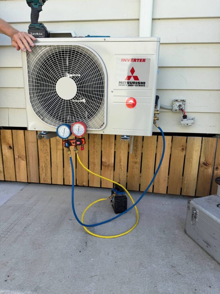 Technician commissioning a Mitsubishi Heavy Industries air conditioning outdoor unit with a vacuum pump and gauges