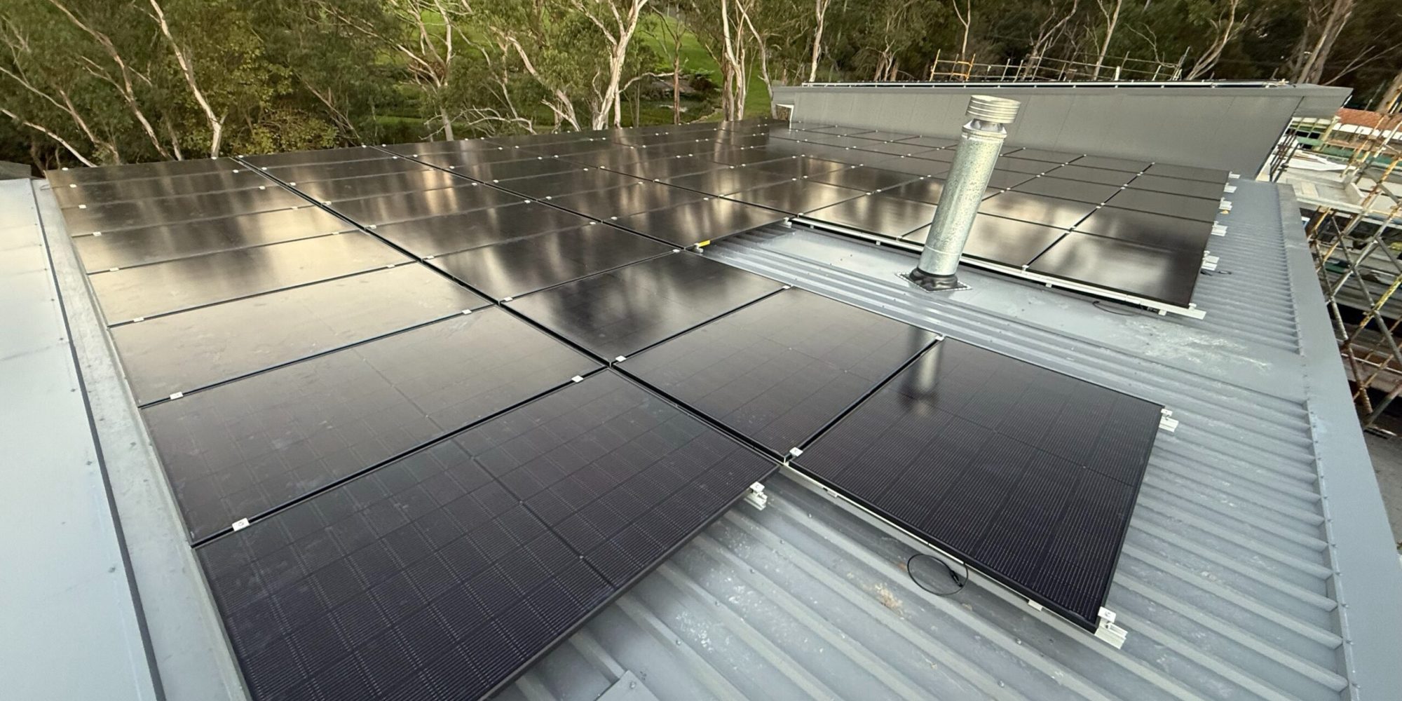 Close-up of sleek black solar panels installed on a residential rooftop surrounded by trees.