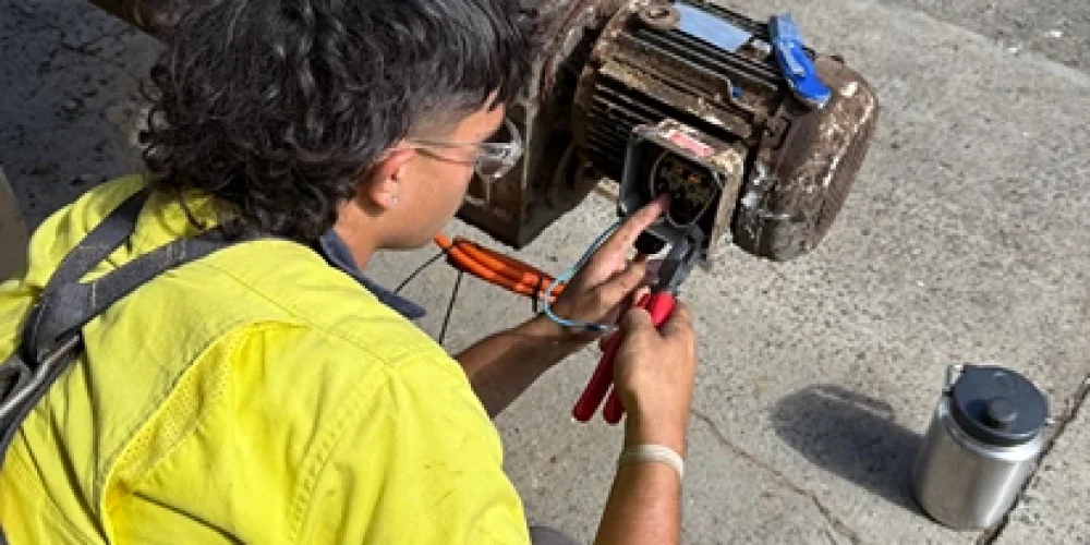 Electrician performing maintenance work on residential electrical with equipment, wearing high-visibility safety gear.