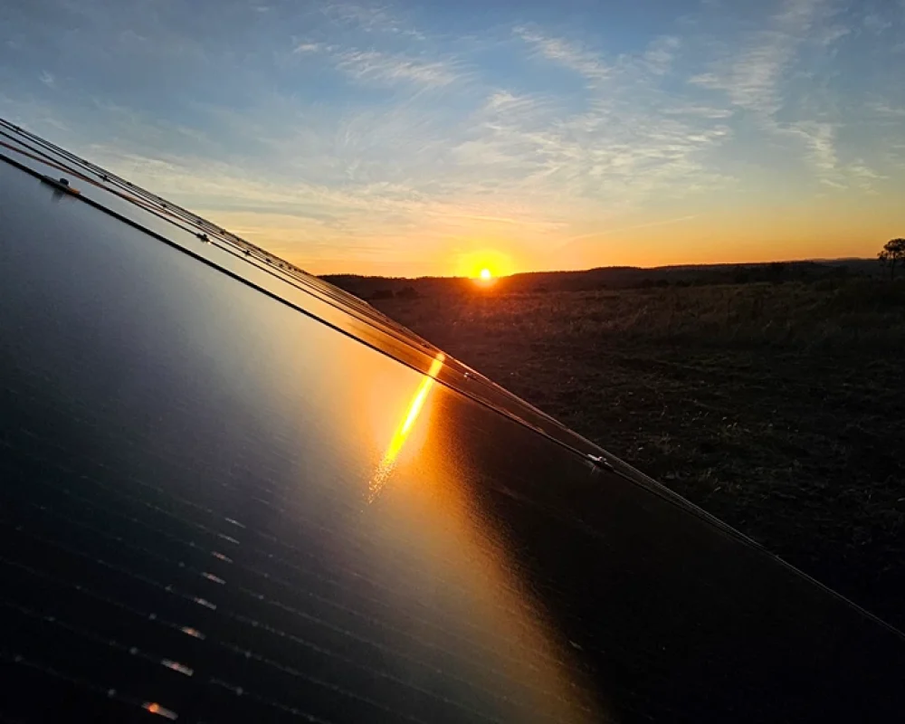 Clean solar panel reflecting a vibrant sunset over a rural landscape.