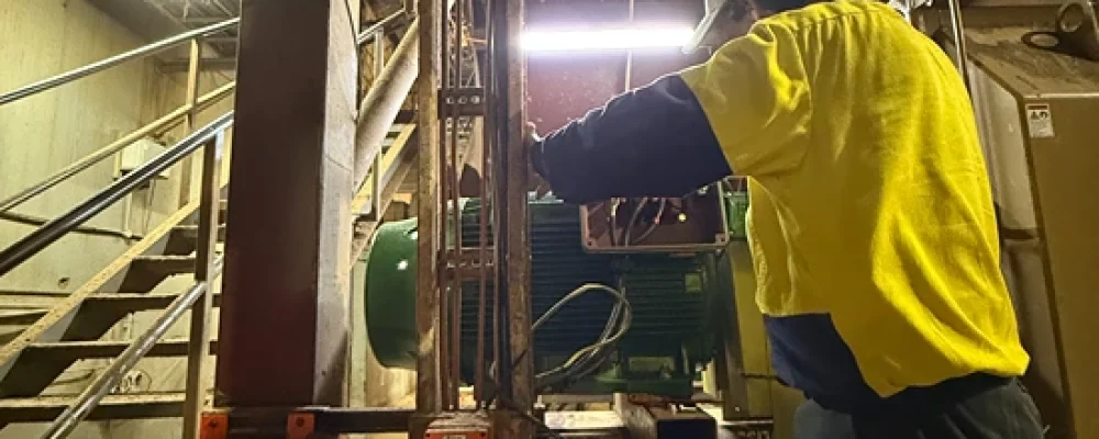 Technician servicing industrial electrical panels in a warehouse, showcasing preventative maintenance in action.